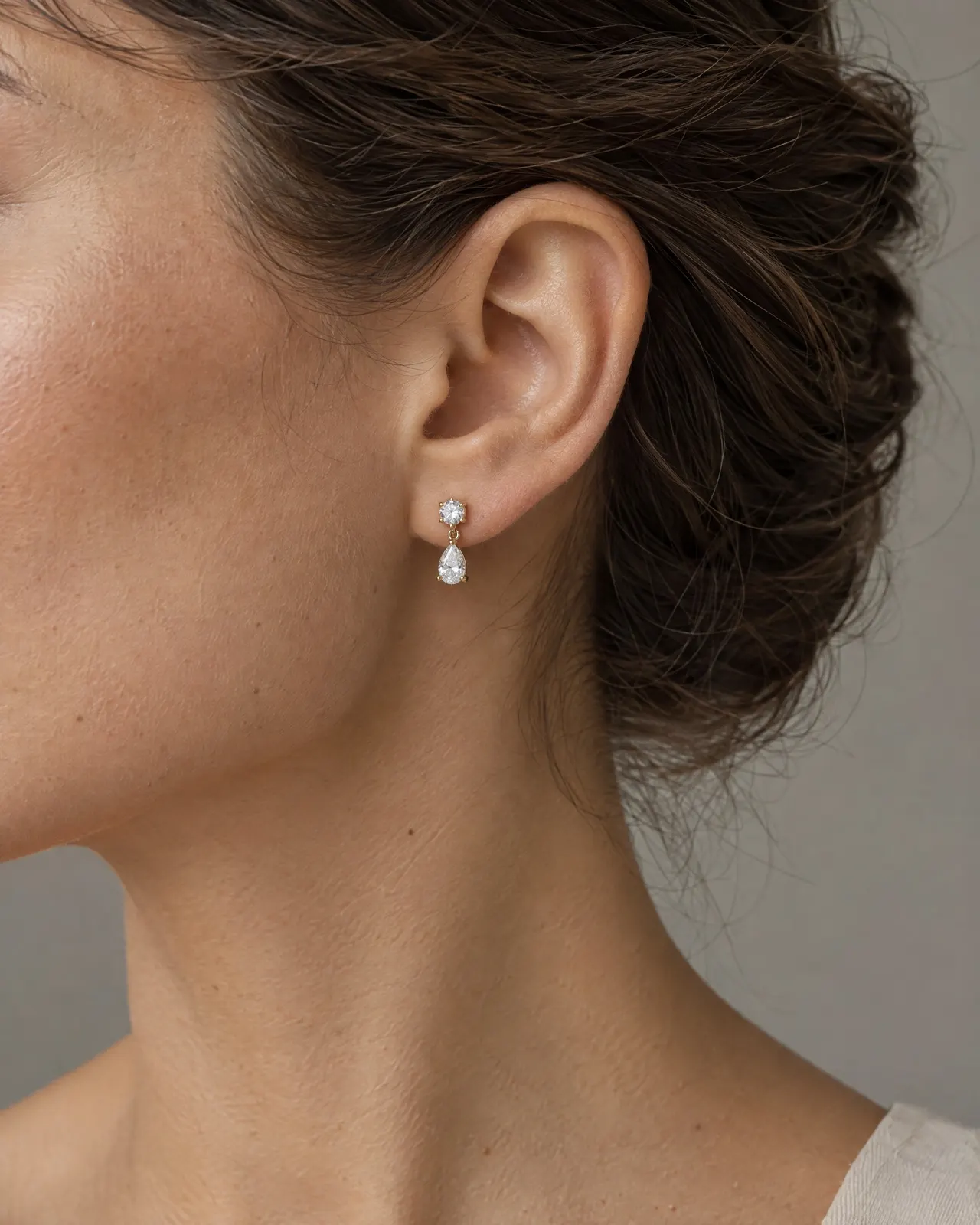 Oreille d'une femme aux cheveux bruns relevés, portant une boucle en or jaune : un petit diamant rond et une goutte de diamant taille poire