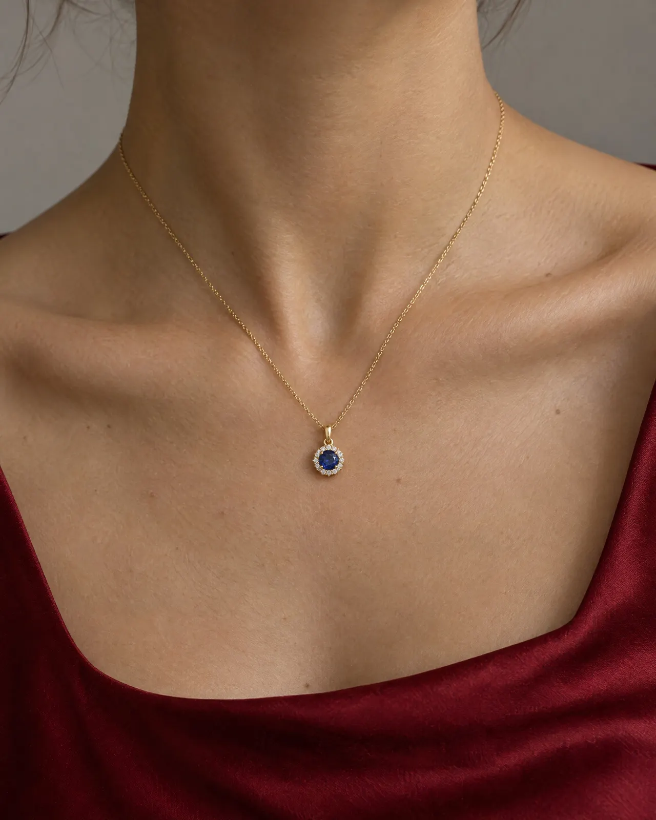 Cou d'une femme en haut de soie cramoisi, portant une fine chaîne en or jaune et un pendentif saphir entouré de petits diamants